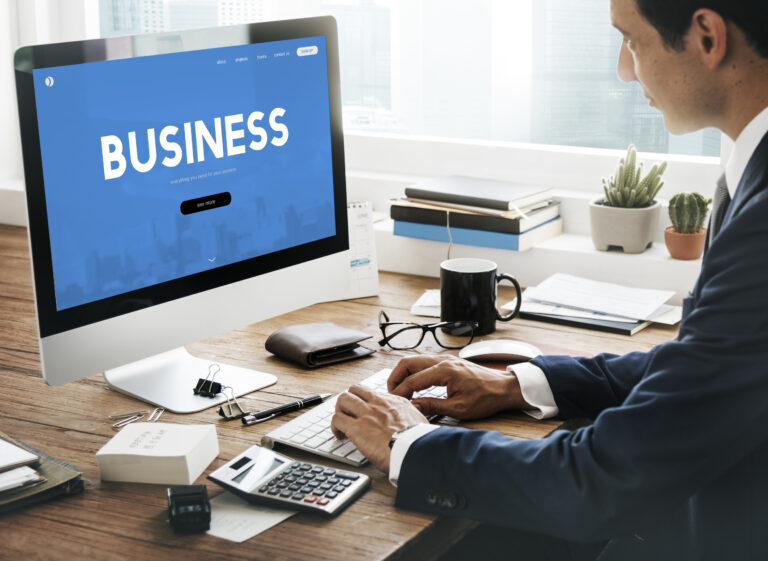 Ejecutivo en su oficina trabajando en un ordenador con un sitio web azul en pantalla para potenciar la web corporativa como herramienta comercial.
